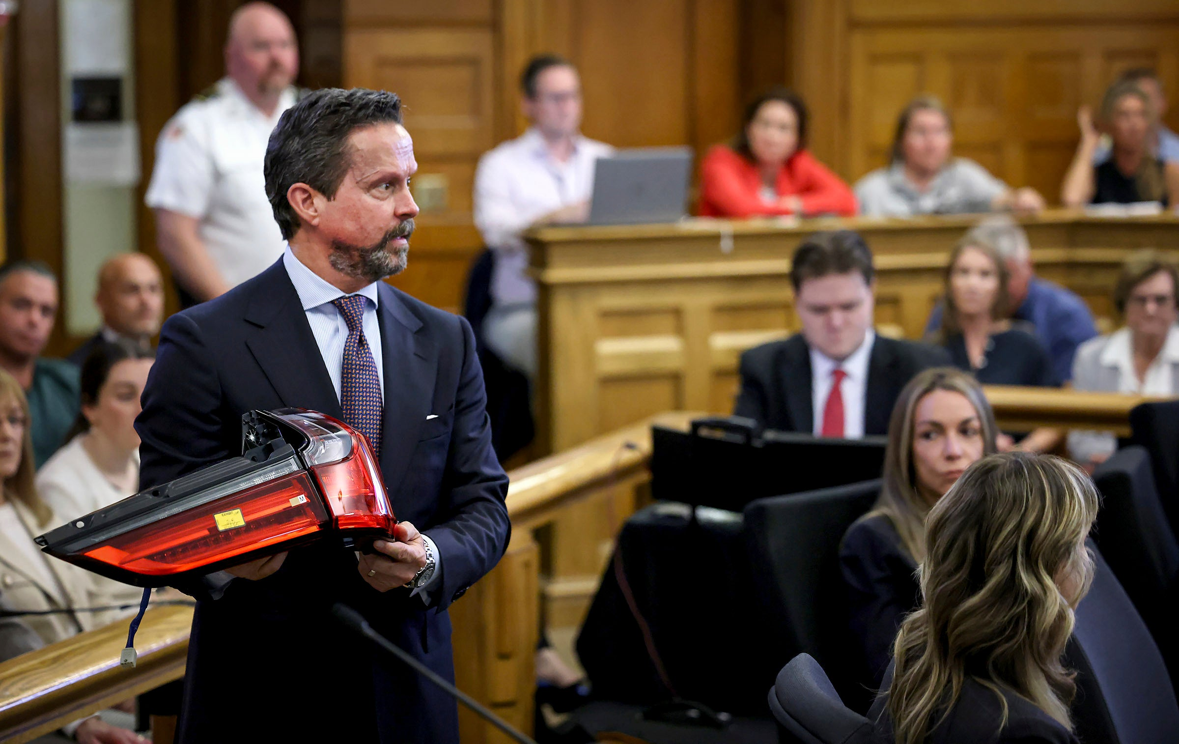 Counsel holding a red-and-clear taillight assembly in a courtroom.