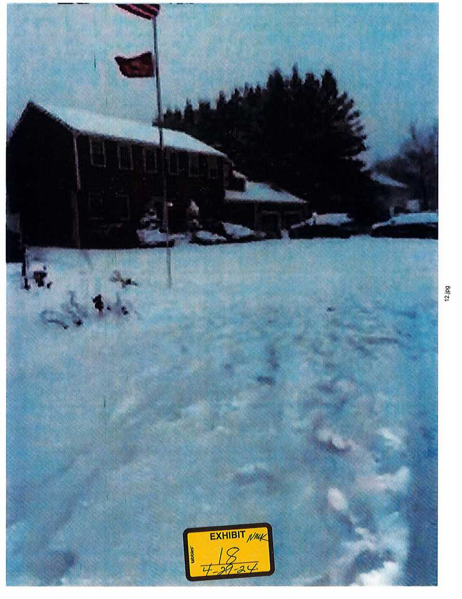 Snow-covered lawn, flagpole and house, with a 2024 exhibit 18 sticker.