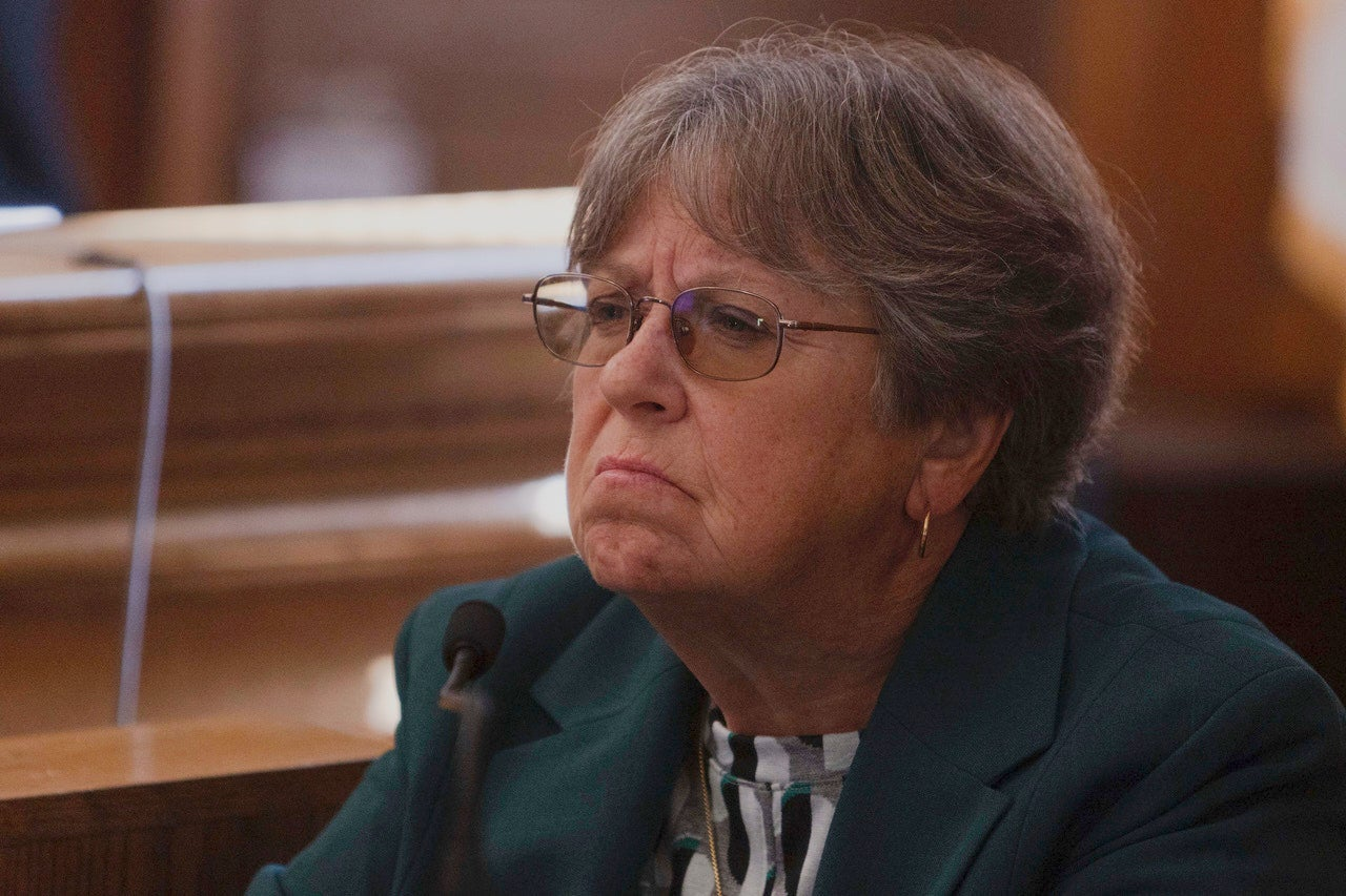 A witness with short gray hair and glasses at a courtroom microphone.