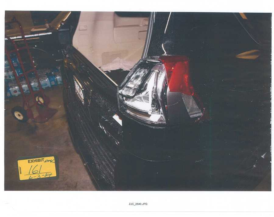 Damaged rear taillight on a dark vehicle inside a garage, with 2024 exhibit sticker 161.